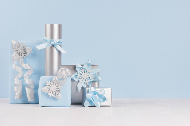 Slavnostní vánoční různé zasněžené dárkové krabičky v světle modré pastelové barvy se stříbrnou stuhy na bílé dřevo stůl. - Fotografie, Obrázek