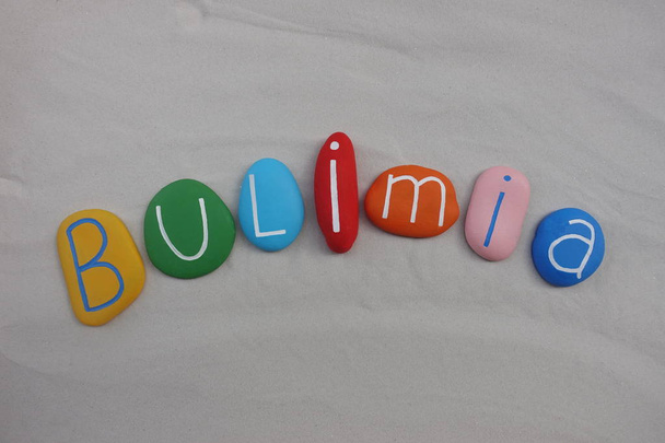 Bulimia texto de la enfermedad con piedras de colores sobre arena blanca
 - Foto, Imagen
