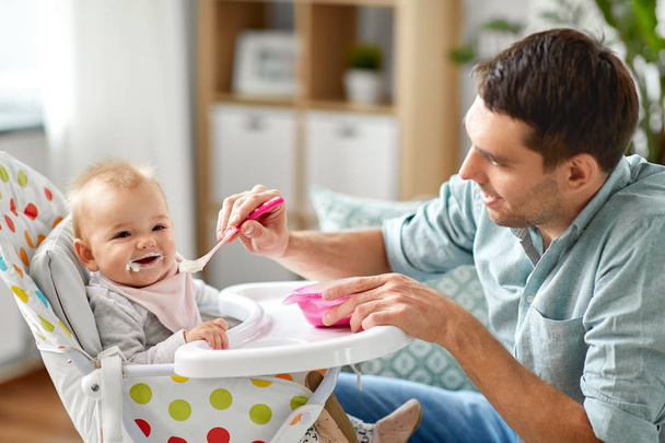 father feeding happy baby in highchair at home - Foto, imagen
