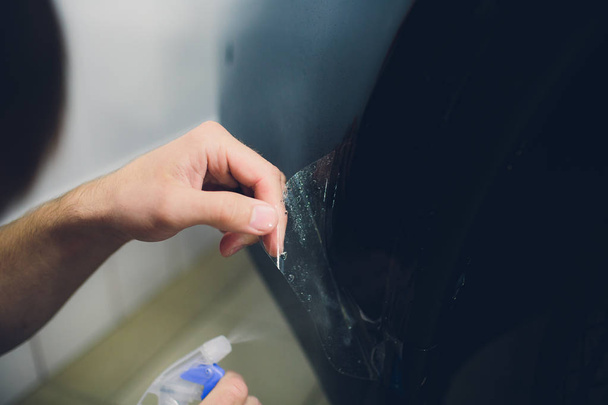 Рука працівника встановлює захисну плівку для фарби автомобіля
 - Фото, зображення