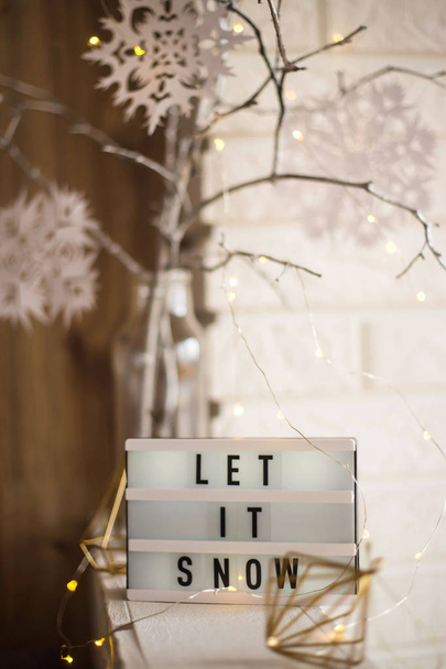 Let it snow it is written on a decorative lamp next to a home winter decor with a vase with tree branches with paper snowflakes against a brick wall of an apartment - Foto, imagen