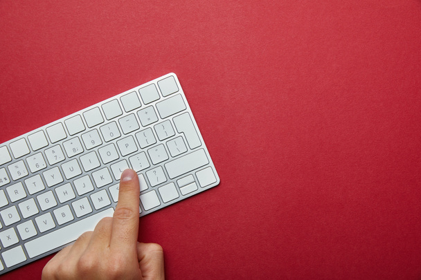 Przycięte widok człowieka, naciskając przycisk na klawiaturze komputera biały na czerwonym tle  - Zdjęcie, obraz