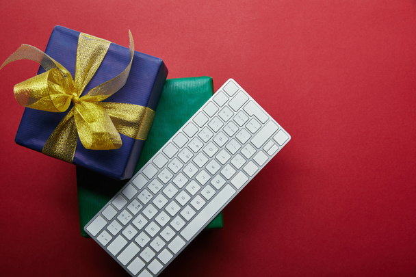 Vue de dessus des cadeaux colorés près du clavier d'ordinateur blanc sur fond rouge
  - Photo, image