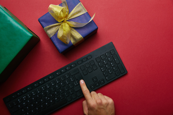 Cropped view of man pushing button on computer keyboard near wrapped boxes on red background  - Foto, Bild