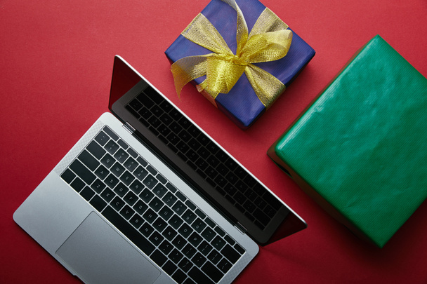 Cropped view of laptop near wrapped gifts on red background  - Фото, изображение