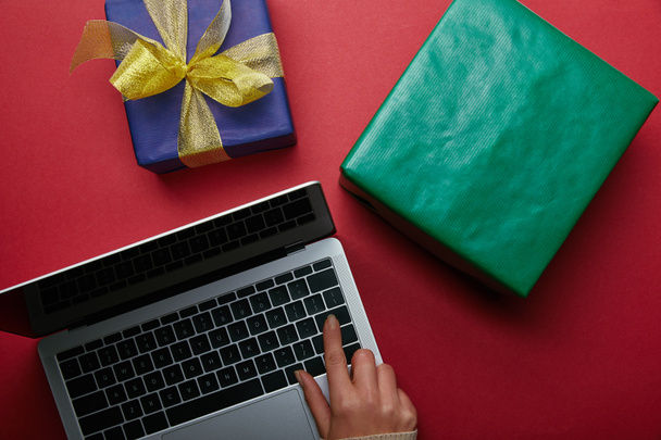 Top view of woman using laptop keyboard near gifts on red background  - Foto, afbeelding
