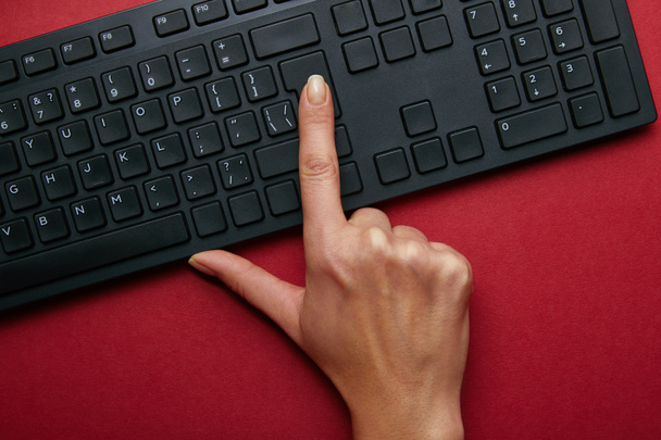 Top view of woman pushing button on black computer keyboard on red background  - Foto, Imagem