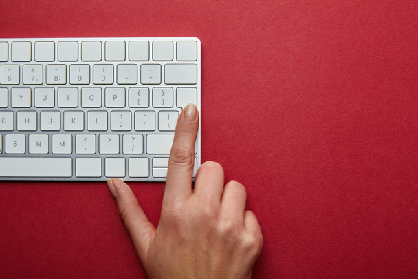 Περικοπεί άποψη της γυναίκας που ωθεί το κουμπί στο πληκτρολόγιο του υπολογιστή σε κόκκινο φόντο  - Φωτογραφία, εικόνα