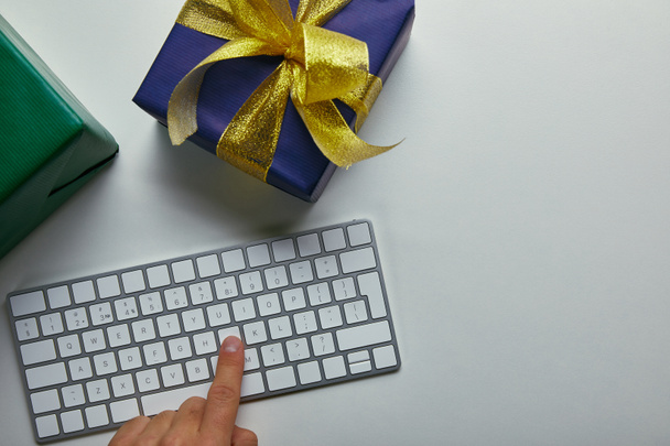 Cropped view of man pushing button on computer keyboard near colourful presents on grey background  - Foto, imagen