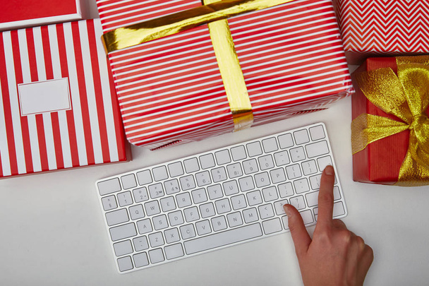 Top view of woman pushing button on computer keyboard near presents on white background  - Φωτογραφία, εικόνα