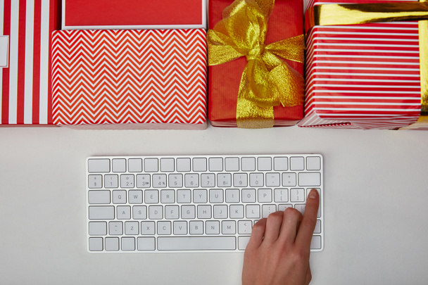 Top view of woman pushing button on computer keyboard near presents on white background  - Фото, зображення