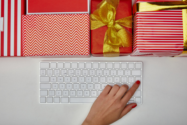 Top view of woman pushing button on computer keyboard near colourful gifts on white background  - Photo, Image