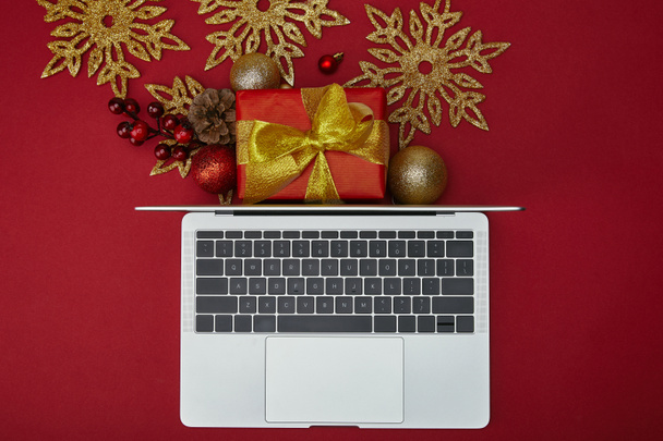 Top view of laptop near wrapped gift and decorations on red background - Foto, immagini