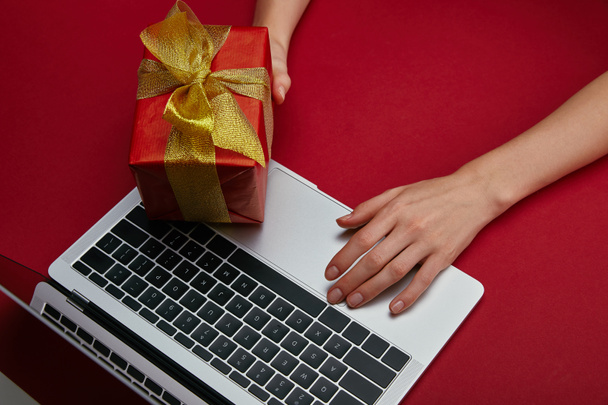 Cropped view of woman holding present near laptop on red background  - Foto, immagini