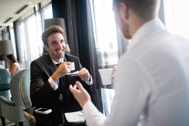 Image of young businessman with cup of coffee communicating with his colleague - Photo, Image
