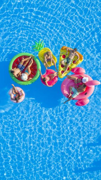 AERIAL TOP DOWN COPY SPACE: підходить для дівчаток і хлопців, які лежать на барвистих бочках у басейні. Щасливі друзі насолоджуються літніми канікулами на надувних ананасах, піці, фламінго, кавуні та пончиках
 - Фото, зображення
