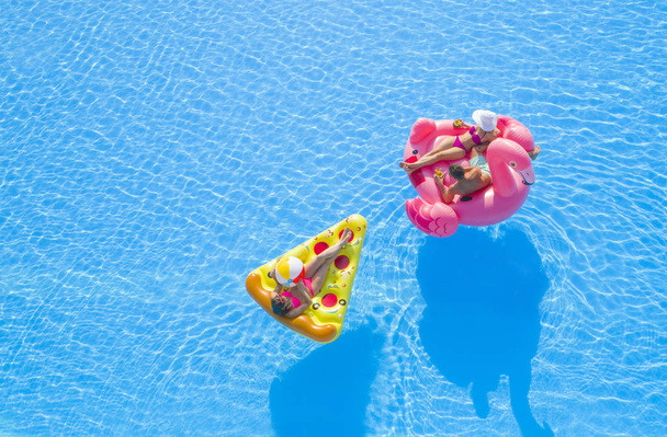 AERIAL CLOSE UP Красива пара і підійде дівчині, що лежить на веселому барвистому надувному плаву, насолоджуючись спокійною літньою відпусткою на курорті. Друзі охолоджують, посипають напої та сонячні ванни на плаву в басейні
 - Фото, зображення