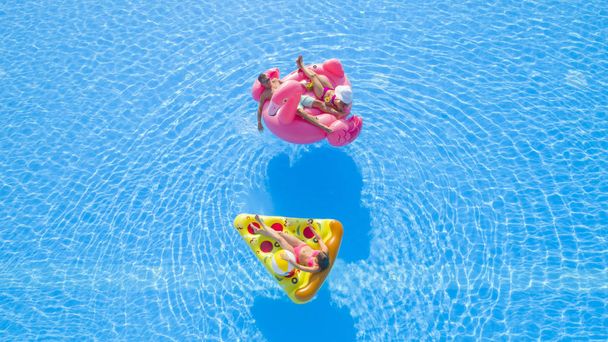 Aerial Close Up Gyönyörű pár és fitt lány fekszik szórakoztató színes felfújható úszók, élvezi a pihentető nyári vakáció üdülőhelyen. Barátok lazulnak, iszogatnak és fürdőznek a medencében. - Fotó, kép