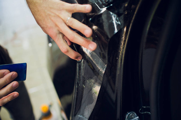 Worker hands installs car paint protection film wrap. - Фото, изображение