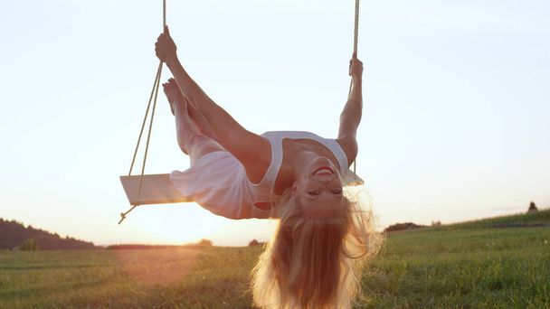 LENS FLARE, CLOSE UP : Une jeune femme séduisante se penche sur le swing tout en se balançant dans une nature dorée. Soleil brillant brillamment sur jeune femme s'amusant à l'extérieur, balançant sur la balançoire d'arbre
 - Photo, image