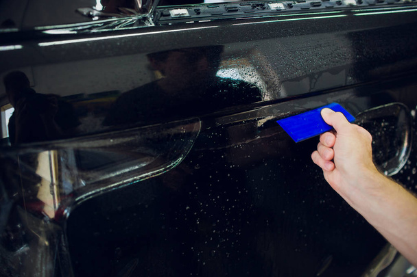 Worker hands installs car paint protection film wrap. - Photo, image