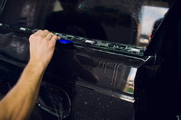 Worker hands installs car paint protection film wrap. - Foto, afbeelding
