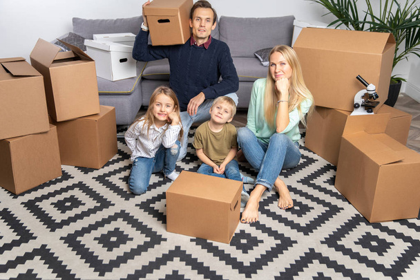 Foto de padres e hijos arriba entre cajas de cartón sentados en el suelo
 - Foto, imagen