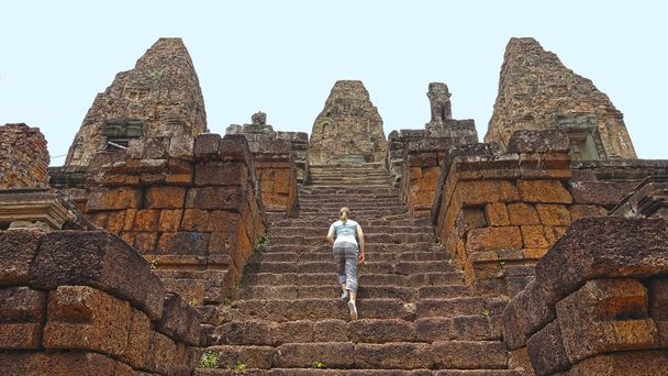 Young female tourist climbing up the stairs of the sacred Angkor Wat temple. House of god Vishnu located in Cambodia. Adventurous woman exploring the local monument. Old Angkor Wat temple in Cambodia. - Photo, Image