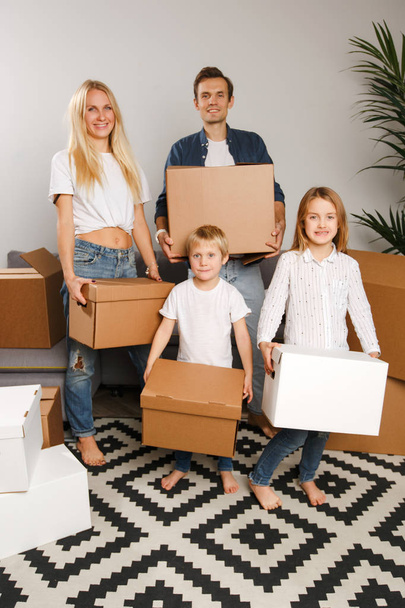 Full-length photo of young married couple with children with cardboard boxes in their hands standing - Photo, Image