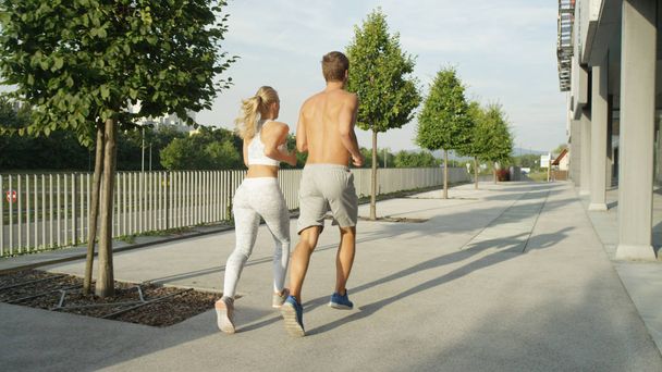 Unrecognizable young man and woman with athletic physiques working out together on a tranquil sunny afternoon. Fit young couple bonds through exercising outdoors on a warm summer day in small city. - Φωτογραφία, εικόνα