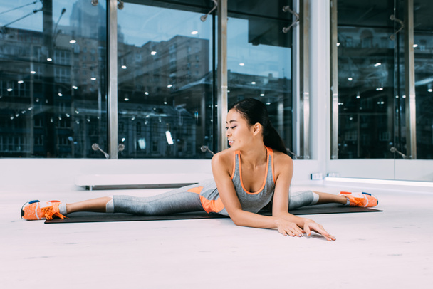 sonriente asiático chica haciendo split en fitness mat en gimnasio
 - Foto, imagen