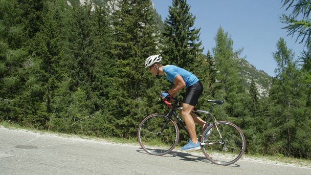 Mladí silniční cyklista chlap dobije strmý asfaltovou silnici směrem k cílové čáře. Odhodlané sportovce pedály do kopce během vyčerpávající cyklistický závod v krásných horách. Úžasné cvičení venku. - Fotografie, Obrázek