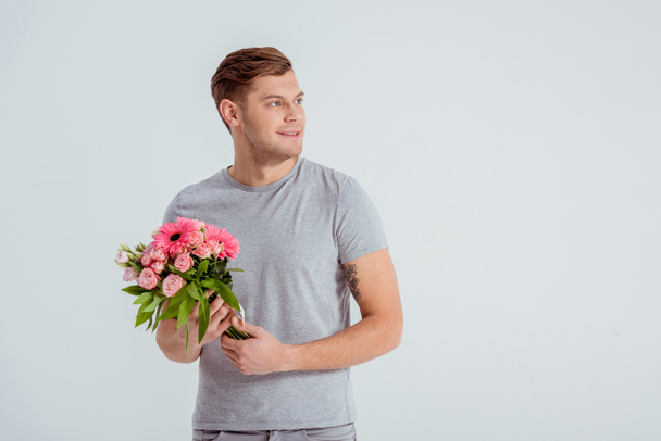 όμορφος άνδρας κρατώντας ροζ λουλούδι μπουκέτο και αναζητούν μακριά απομονωμένες σε γκρι - Φωτογραφία, εικόνα