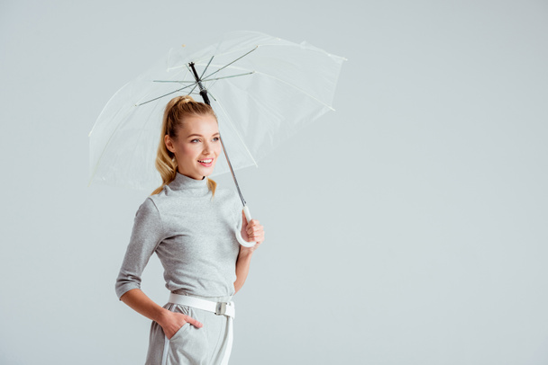 szép nő, a szürke ruhákat és a kezét a zsebében jelentő elszigetelt szürke átlátszó esernyő - Fotó, kép