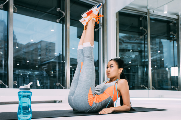 atractivo asiático chica mintiendo y levantando piernas hasta en fitness mat en gimnasio
 - Foto, Imagen