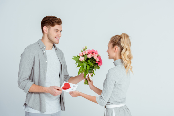 man greeting woman with Valentines card and flower bouquet isolated on grey - Foto, Imagem