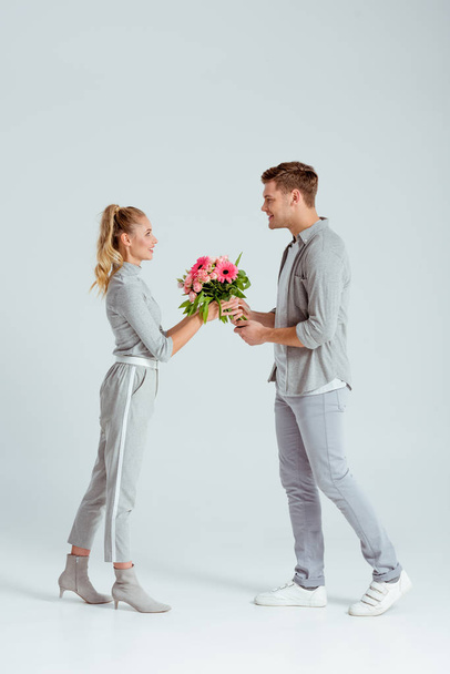 smiling man giving pink flower bouquet to woman isolated on grey background - Photo, Image