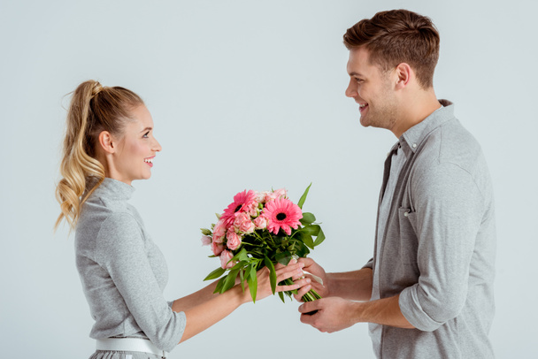 man giving pink flower bouquet to beautiful woman isolated on grey - Fotografie, Obrázek