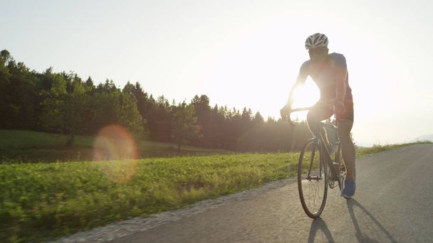 コピー スペース、レンズフレア: プロ男性道のバイカーは彼の自転車で日当たりの良いクルーズを楽しんでします。日当たりの良い春の田園地帯を通ってプロ自転車ロードレースのレースのサングラスと活発な男性. - 写真・画像