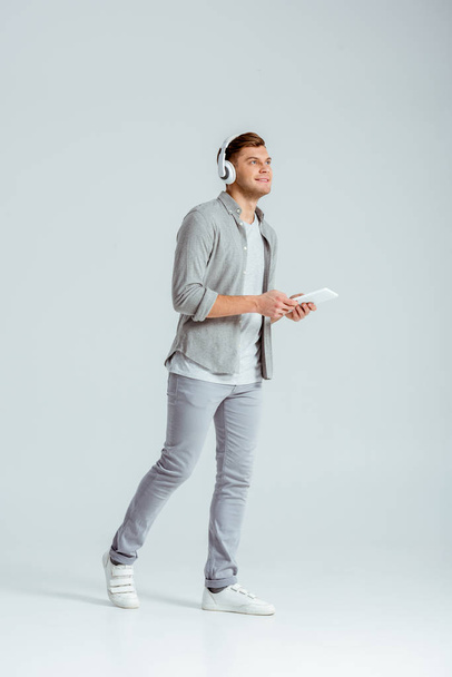 Muž na sobě sluchátka, poslech hudby a používání digitálních tabletu na šedém pozadí - Fotografie, Obrázek