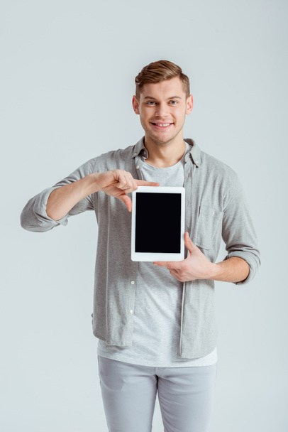 smiling man in grey clothing presenting digital tablet with blank screen isolated on grey - Foto, imagen