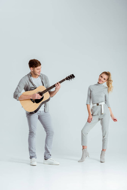 man playing acoustic guitar while smiling woman dancing on grey background - Foto, Imagem