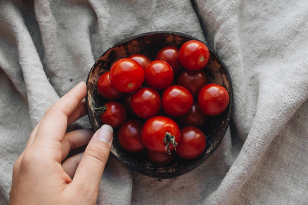 female hand taking tomato out of rustic bowl - Фото, изображение