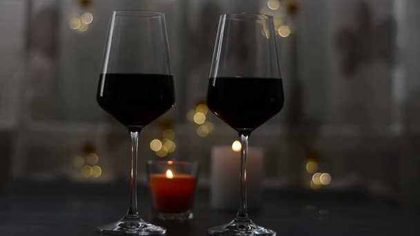 Twee glazen wijn rode staande op een donkere tafel met kaars en slingers - Video