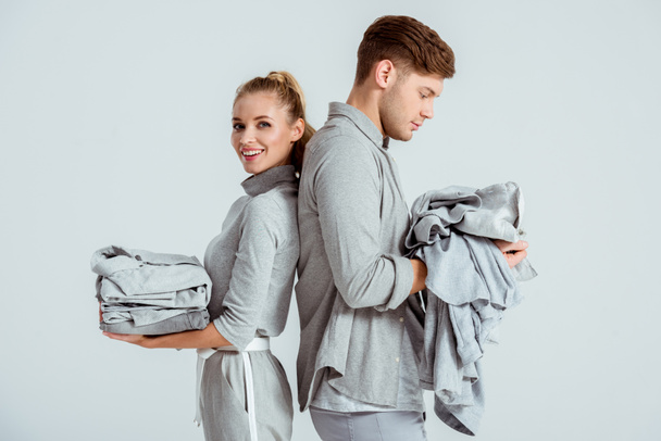 young couple in grey outfits holding grey clothes isolated on grey - Photo, Image