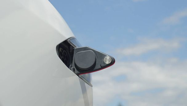 Közelről: Luxus Tesla elektromos autó készen áll a felügyelet Akkumulátorcellák napos ég alatt. Drága fehér elektromos autó töltés. Környezettudatos szállítás jármű bedugott-ban, kitöltése - Fotó, kép