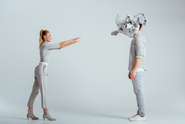blonde woman throwing pile of clothes at man on grey background - Фото, изображение