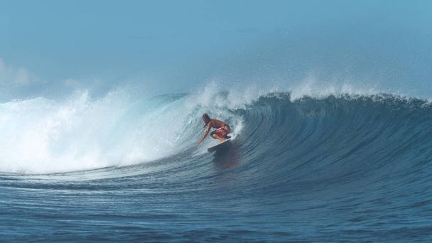 Doświadczonym surferem jeździ na falę big baryłkę krystalicznie czyste popularne surf spot. Niesamowite surfboarder mężczyzna rzeźbi duża fala głęboko niebieski pochodzących z potężnym oceanie. Adrenalina, wypełnione letnich aktywności. - Zdjęcie, obraz