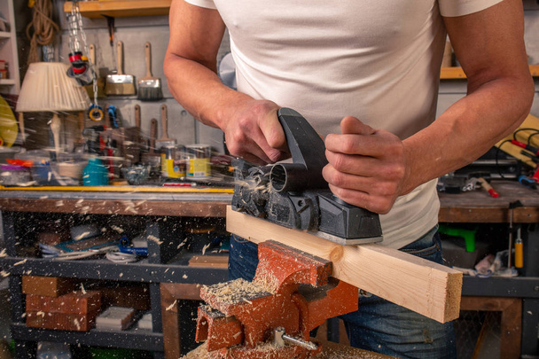 Een timmerman werkt op houtbewerking de machine tool. Meubelen-details zagen met een cirkelzaag. Proces van zaag onderdelen in delen. Tegen de achtergrond van de workshop - Foto, afbeelding