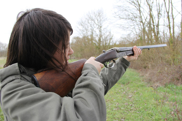 Крупным планом молодая женщина-охотник целится из своего пистолета в поле
. - Фото, изображение